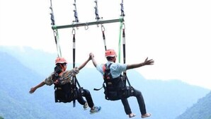 Two people suspended in mid-air, wearing harnesses and helmets, against a mountainous backdrop. - Vista Luxurious Resort & Fun Park (Bhedetar)