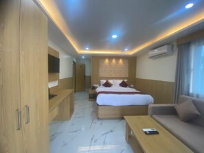 A hotel room with a bed, a sofa, a desk, a wardrobe, and an air conditioning unit. - Vista Luxurious Resort & Fun Park  (Bhedetar)