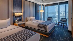 A hotel room with two beds, a small table, chairs, and a large window with a view. - Vista Luxurious Resort & Fun Park (Bhedetar)