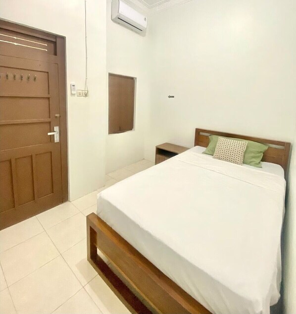 A bedroom with a bed, a wooden headboard, a nightstand, a door, and an air conditioning unit.