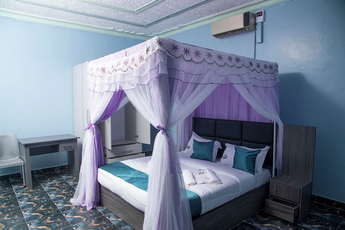 A bedroom with a four-poster canopy bed, a bedside table, a chair, and a wardrobe.