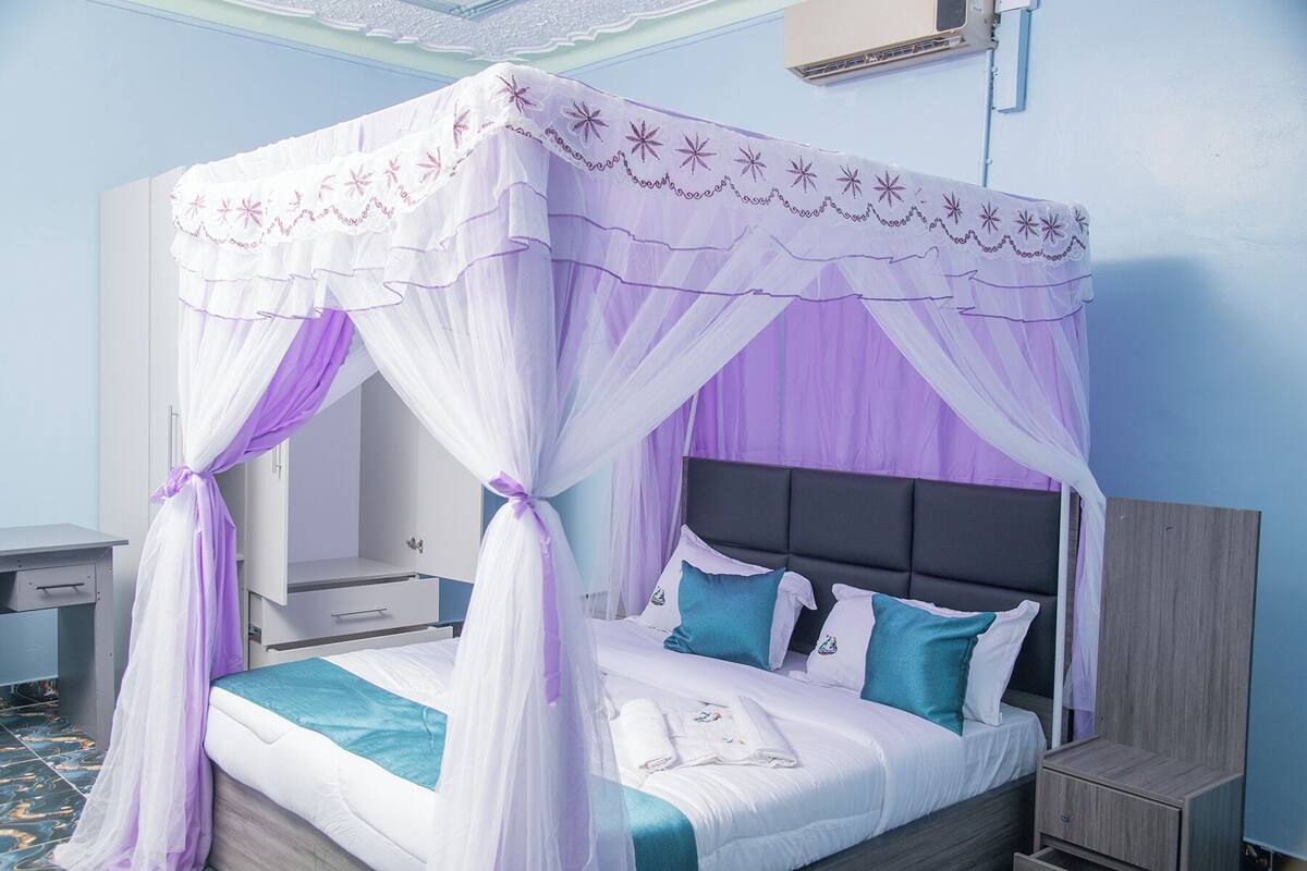 A bed with a canopy, a bedside table, a nightstand, and a wall-mounted air conditioning unit.