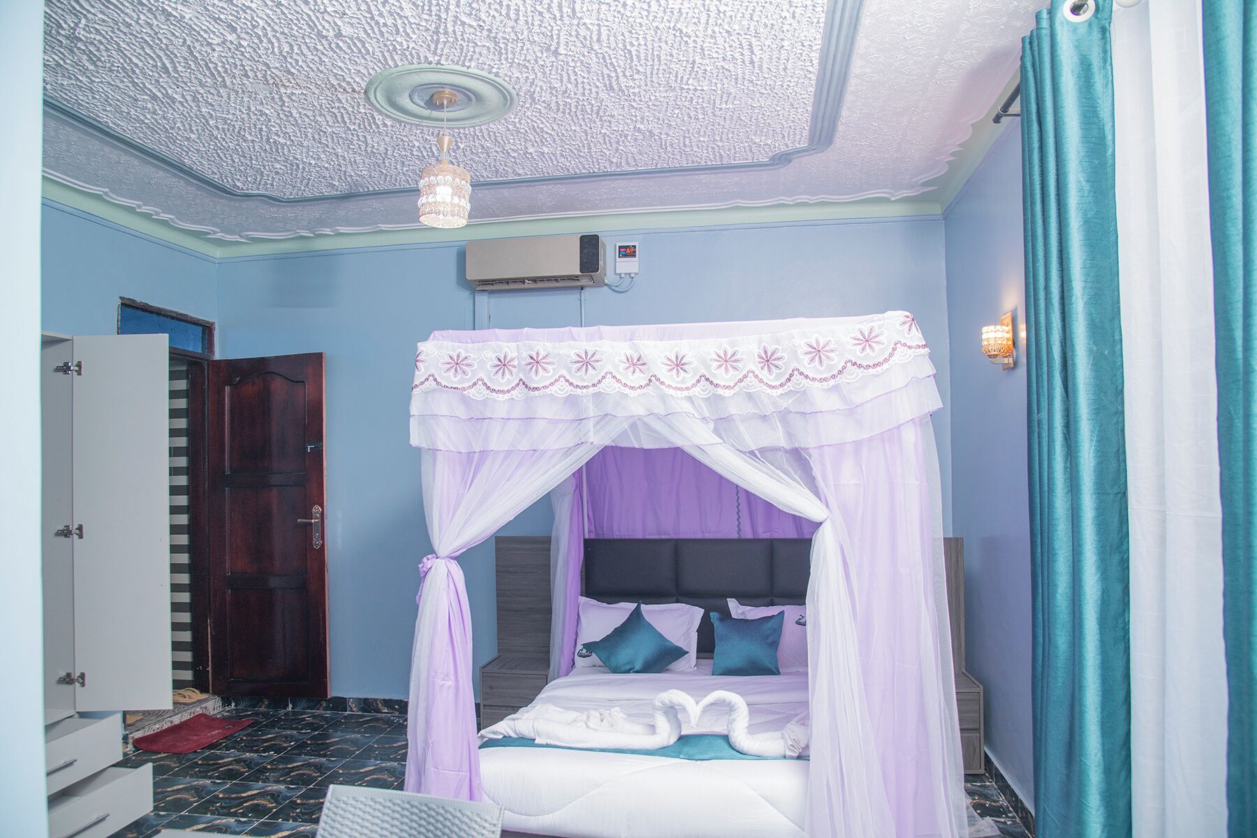 A bedroom with a four-poster bed, a wooden wardrobe, and a ceiling fan.