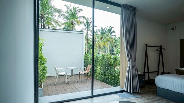 Ein modernes Hotelzimmer mit einer großen Schiebeglasdoor zum Außenbereich, der einen Tisch und Stühle, ein Bett und eine Garderobe bietet.