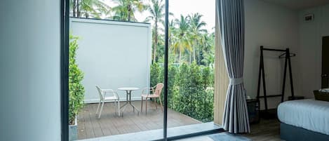 A modern hotel room with a large sliding glass door leading to an outdoor area with a table and chairs, a bed, and a hanging rack.