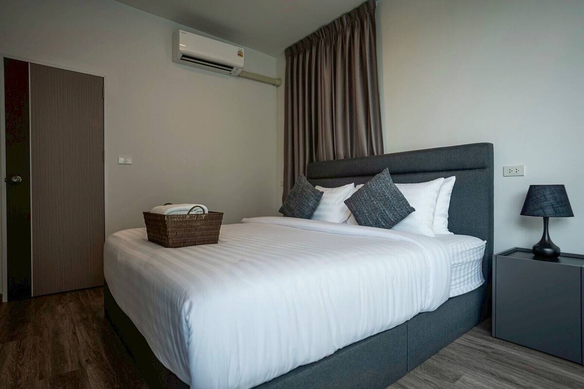Une chambre d’hôtel comprenant un lit, une table de chevet, une lampe, un appareil de climatisation et une porte.