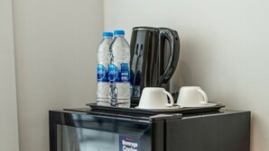 Ein kompakter Kühlschrank mit Getränkekühler, zwei Wasserflaschen, einer Kaffeemaschine und zwei weißen Tassen auf der Oberseite.