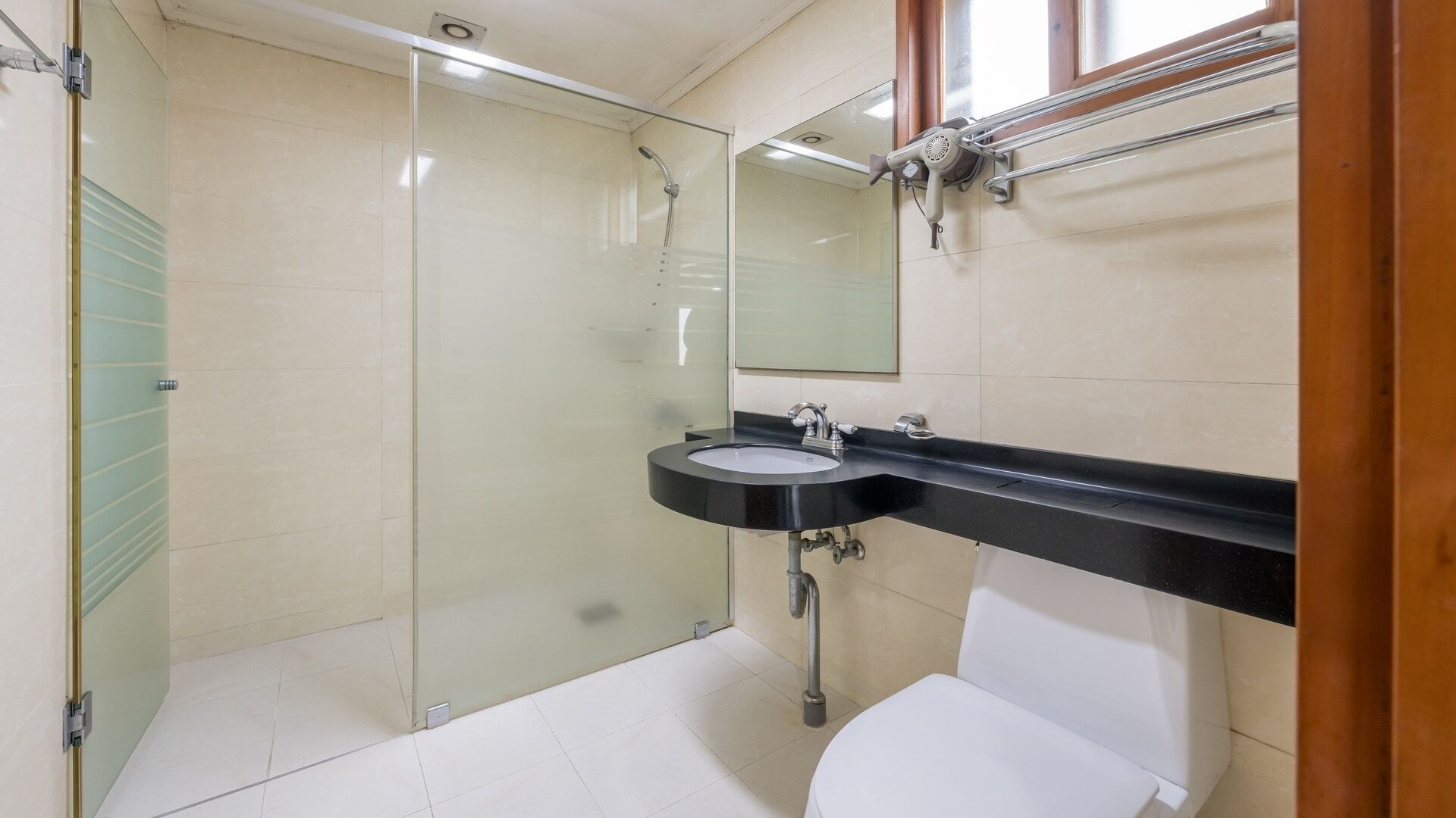 A bathroom with a glass shower enclosure, a sink with a black countertop, and a white toilet.