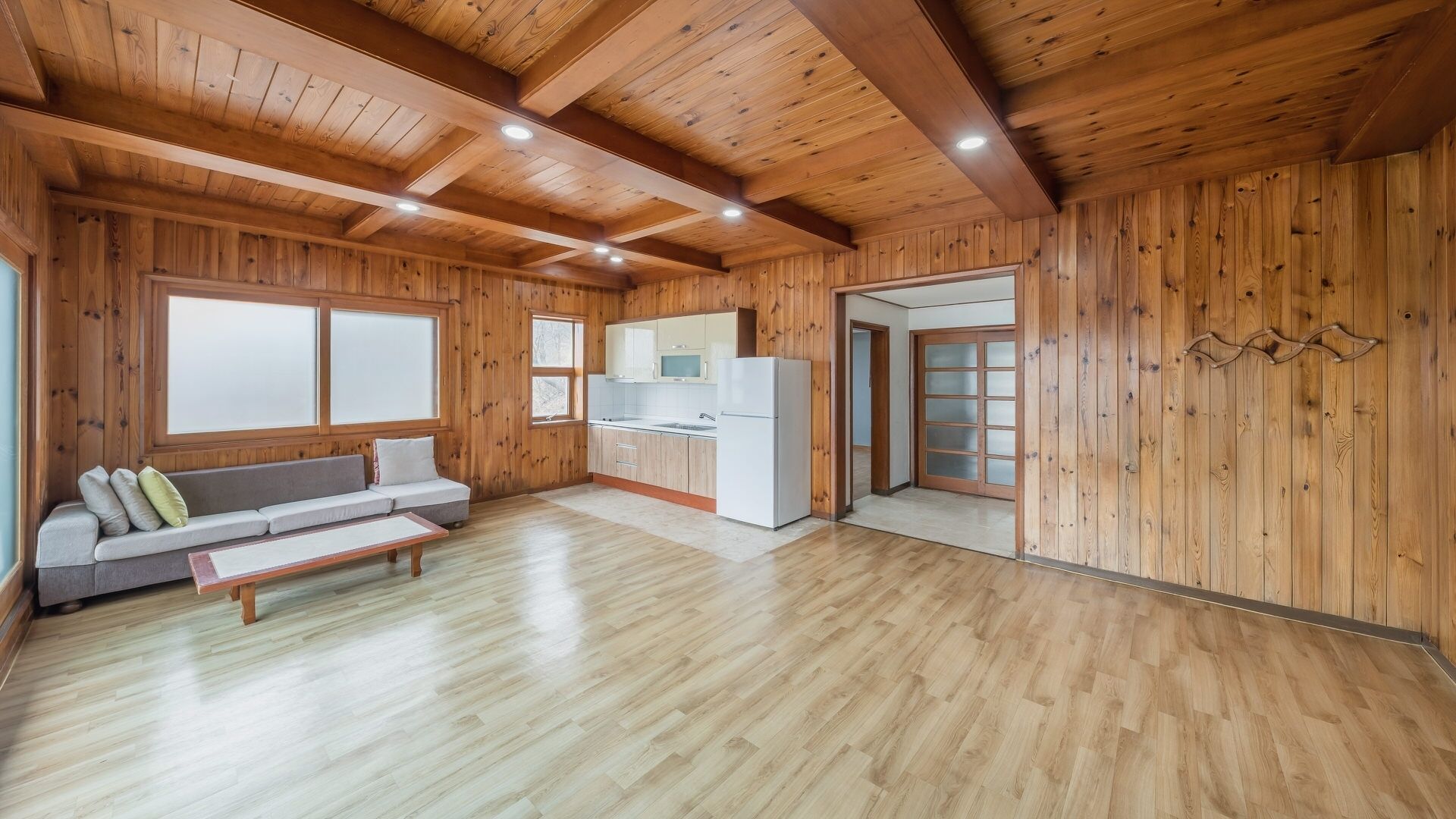 Una stanza spaziosa con pareti e soffitto in legno, un angolo cottura, un divano con cuscini e una panca.
