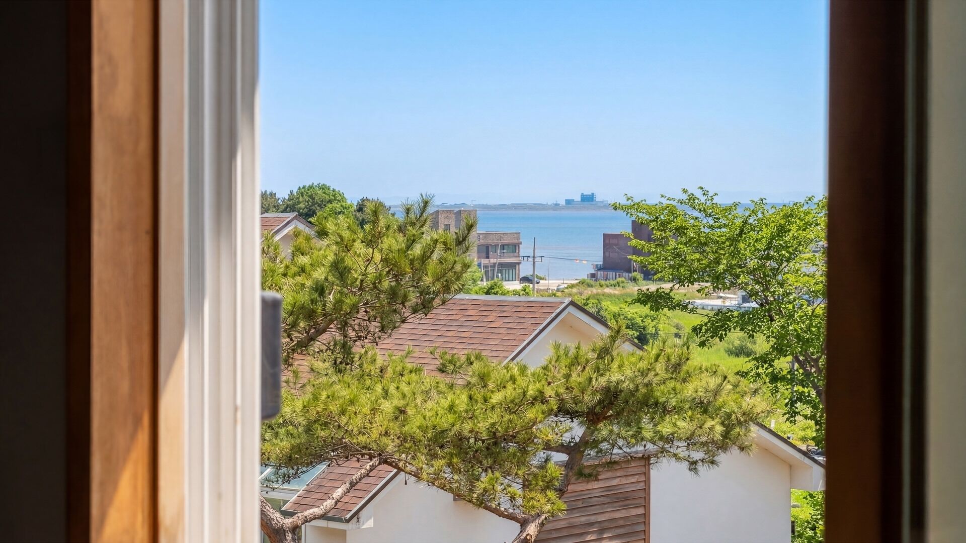 A view through a window of a residential area with houses, trees, and a body of water in the distance.