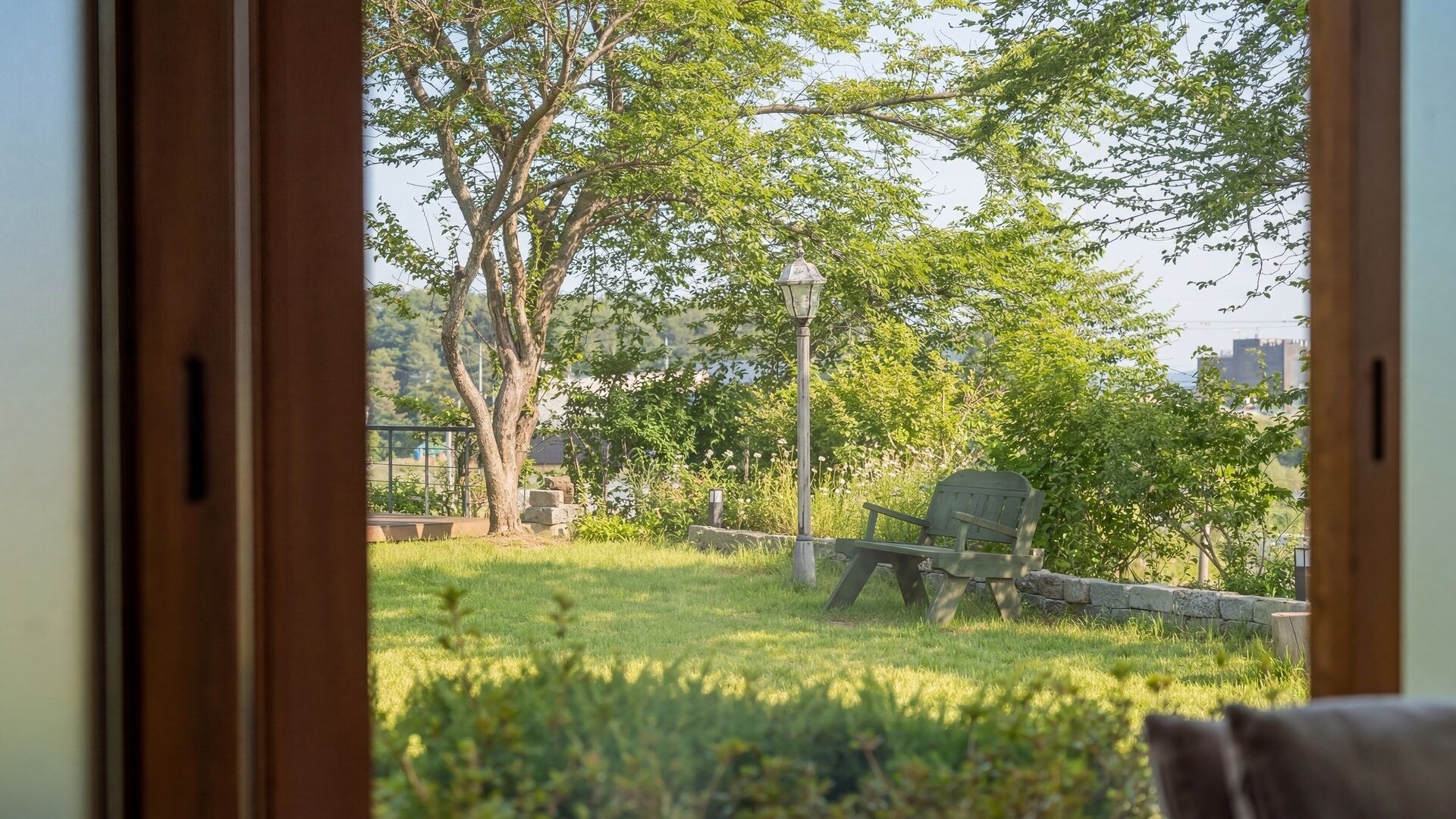 A view through a window of a park with a bench and a lamp post.