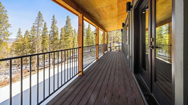 Un terrazzino in legno con ringhiera, ampie finestre e vista sugli alberi.