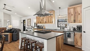Una cucina moderna con isola centrale, mobili in legno, elettrodomestici in acciaio inossidabile e una ventola a soffitto.