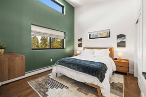 Une chambre à coucher comprenant un lit, des tables de chevet, une commode, une fenêtre avec vue et des œuvres d’art accrochées au mur.