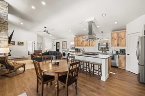 A modern kitchen with wooden cabinets, a central island, and a dining area with a wooden table and chairs. - 2BR New Home in Twin Lakes, Views, Pet Friendly (Twin Lakes)