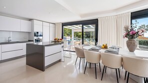 Una cocina moderna con una isla central, comedor con sillas y una mesa, y un ventanal con cortinas.