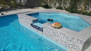 A swimming pool with a tiled edge, a seating area with a fruit bowl and glasses, and a stone wall in the background. - Flora Maris Pool Apartments (Privlaka)