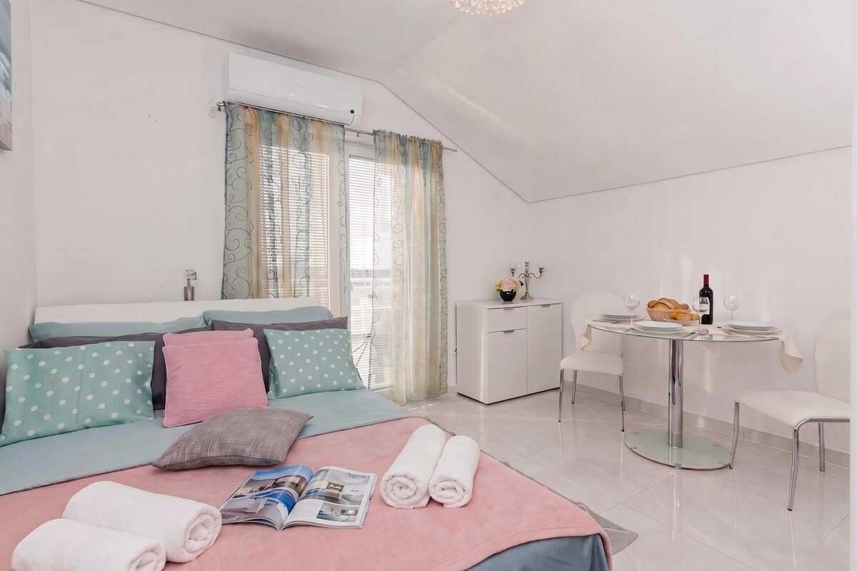 A modern bedroom with a bed, a small desk, and a dining area with a table and chairs.
