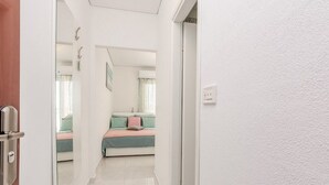 A hallway leading to a bedroom with a bed, a door, and a mirror reflecting the room. - Flora Maris Pool Apartments (Privlaka)