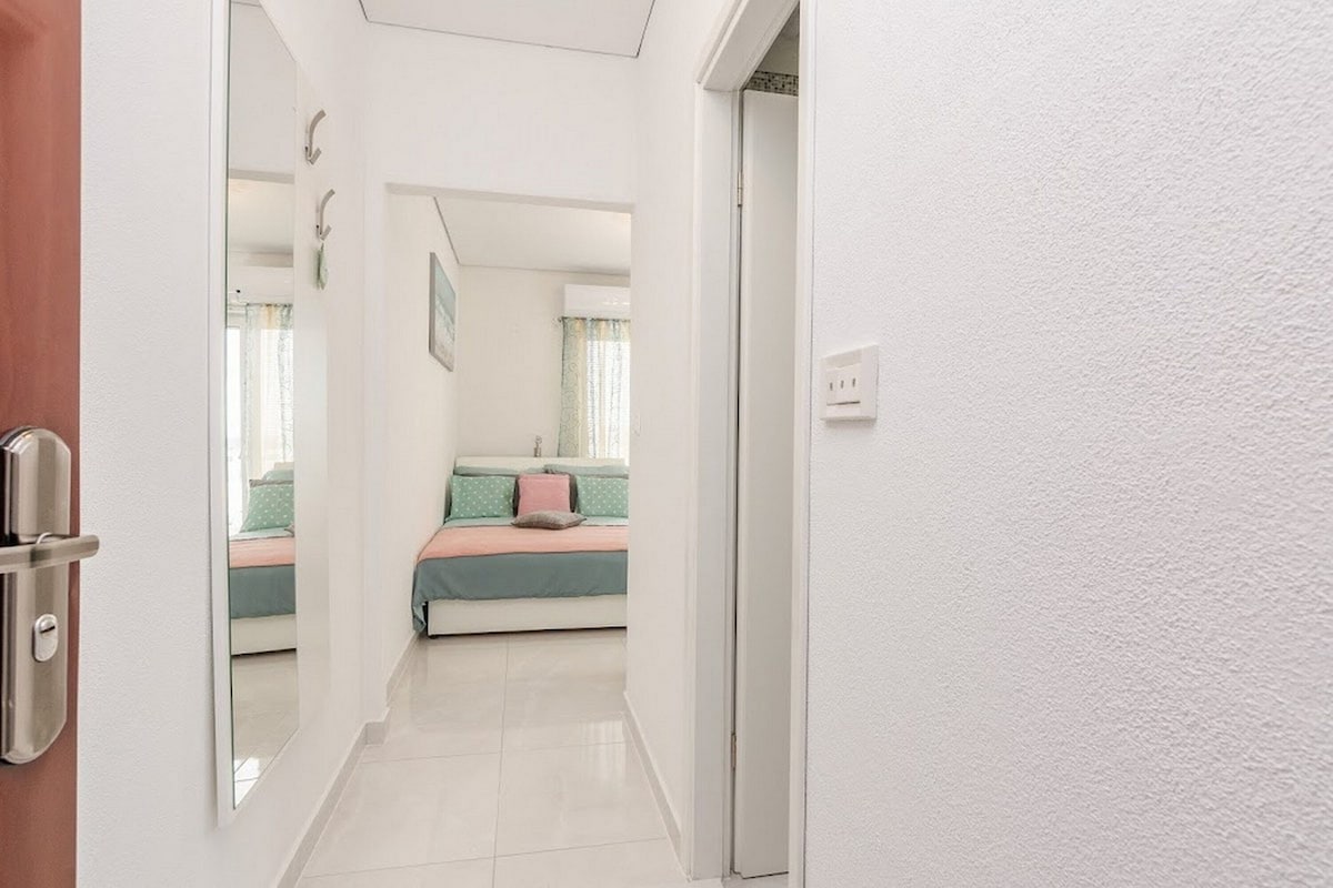 A hallway leading to a bedroom with a bed, a door, and a mirror reflecting the room.