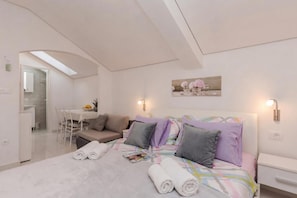 Ein modernes Schlafzimmer mit Bett, Nachttisch, Fenster und einem durchgehenden Türrahmen sichtbarem Badezimmer.
