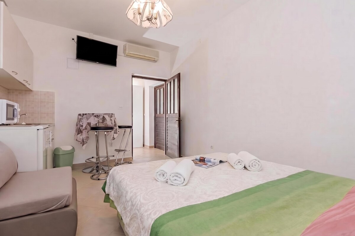 A hotel room with a bed, a TV, a small kitchenette, and a bathroom.