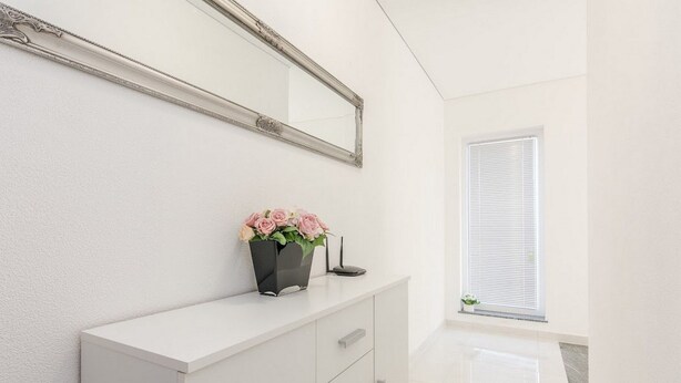 A white vanity with a mirror, a vase with flowers, and a small plant on a white cabinet. - Flora Maris Pool Apartments (Privlaka)