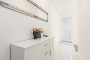 Un tocador blanco con espejo, un florero con flores y una pequeña planta sobre un mueble blanco.