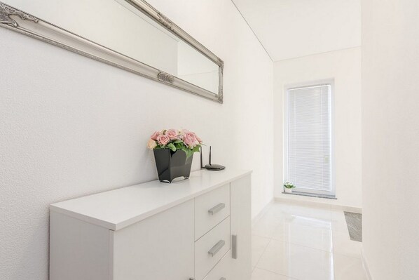 A white vanity with a mirror, a vase with flowers, and a small plant on a white cabinet. - Flora Maris Pool Apartments (Privlaka)