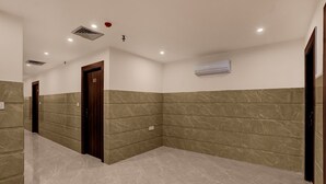 A hallway with marble flooring, a wooden door, and an air conditioning unit on the wall. - Townhouse Subharti University Meerut (Meerut)