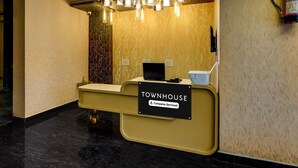 A reception desk with a sign reading 'Townhouse Company-Serviced,' a laptop, a white box, and a fire extinguisher mounted on the wall. - Townhouse Subharti University Meerut (Meerut)