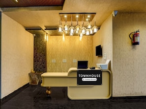 A reception desk with a sign reading 'TOWNHOUSE Company-Serviced,' a fire extinguisher, a security camera, and a decorative light fixture.