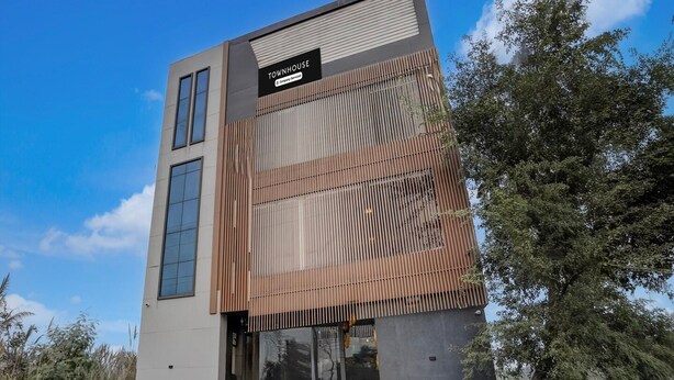 A modern building with a sign reading 'TOWNHOUSE,' featuring a vertical wooden panel design, large windows, and a paved entrance area. - Townhouse Subharti University Meerut (Meerut)