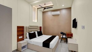 A modern hotel room with a bed, bedside tables, a ceiling fan, an air conditioning unit, a TV, and a small desk. - Townhouse Subharti University Meerut (Meerut)