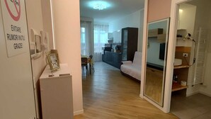 Ein Wohnzimmer mit einer Couch, einem Esstisch mit Stühlen und einer Küche im Hintergrund.