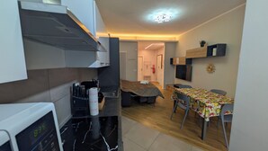 Eine kompakte Küche mit Mikrowelle, Spüle und Herd. Ein Essbereich mit Tisch und Stühlen, und ein Bett im Hintergrund.
