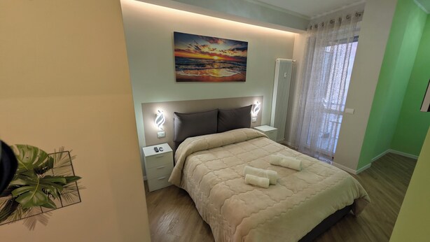 Ein Schlafzimmer mit Bett, Nachttischen, einem Fenster mit Vorhängen und einem Gemälde.