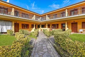 A courtyard with a stone pathway, yellow walls, and a two-story building with balconies. - Residence La Perla Apartments (Monte Isola)