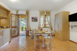 A dining area with a table set for two, a television mounted on the wall, and a sliding door leading to an outdoor area. - Residence La Perla Apartments (Monte Isola)
