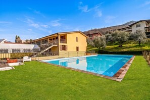 Um imóvel residencial com piscina, gramado bem cuidado e uma casa de dois andares com varanda.