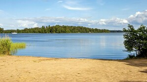 A sandy beach with calm water, a distant tree line, and a sailboat. - 7 Person Holiday Home in Adelso (Adelso)