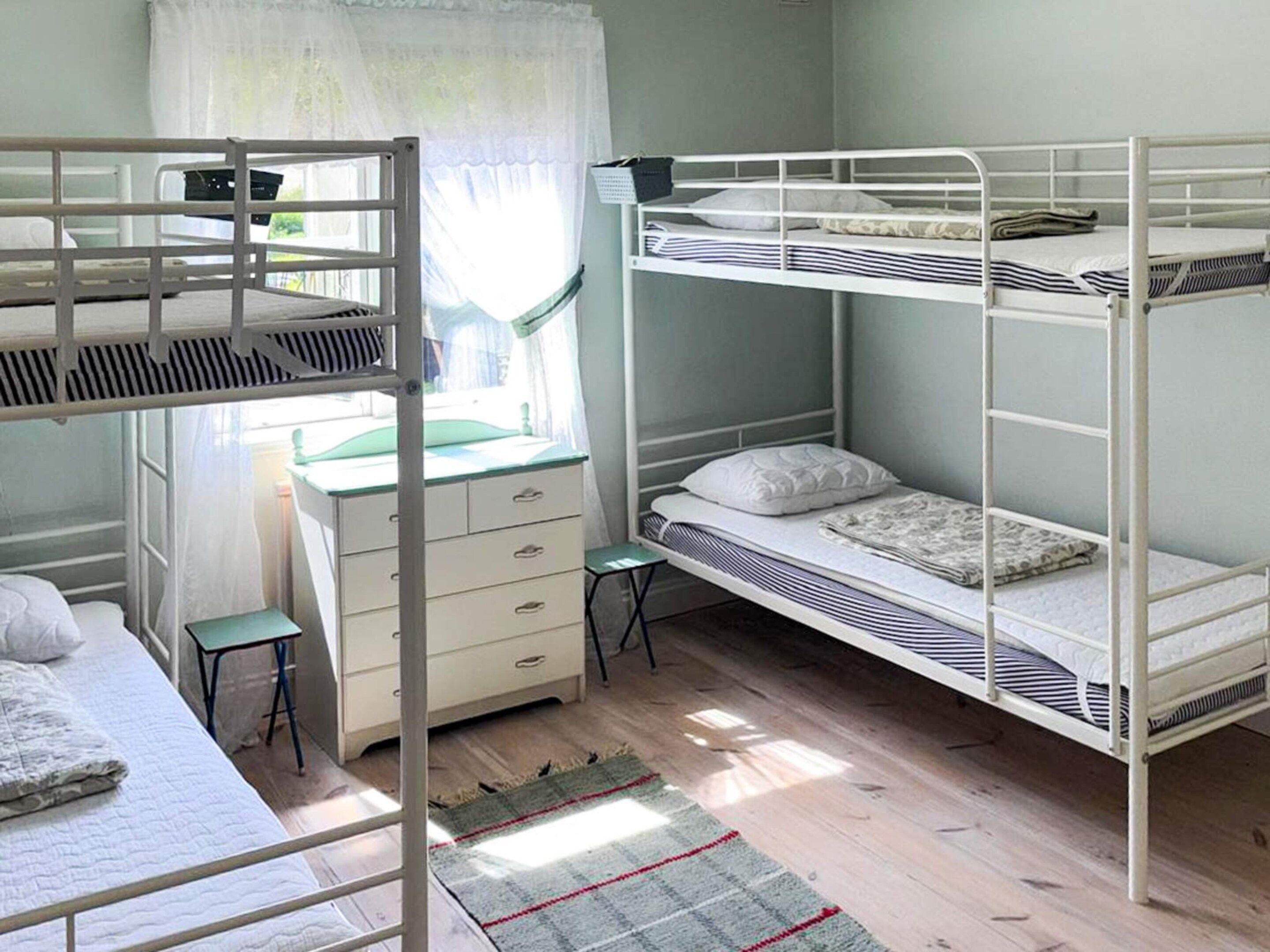 A bunk bed room with a desk and drawers, a small stool, and a window with curtains.