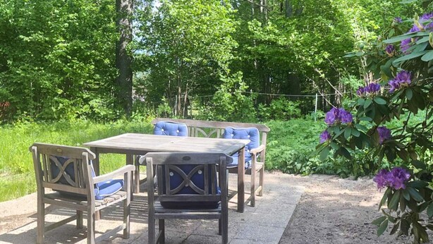 An outdoor patio with a table and four chairs, surrounded by greenery and flowering plants. - 7 Person Holiday Home in Adelso (Adelso)