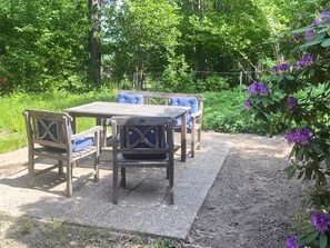 Un patio al aire libre con una mesa y cuatro sillas, rodeado de follaje y plantas en flor.