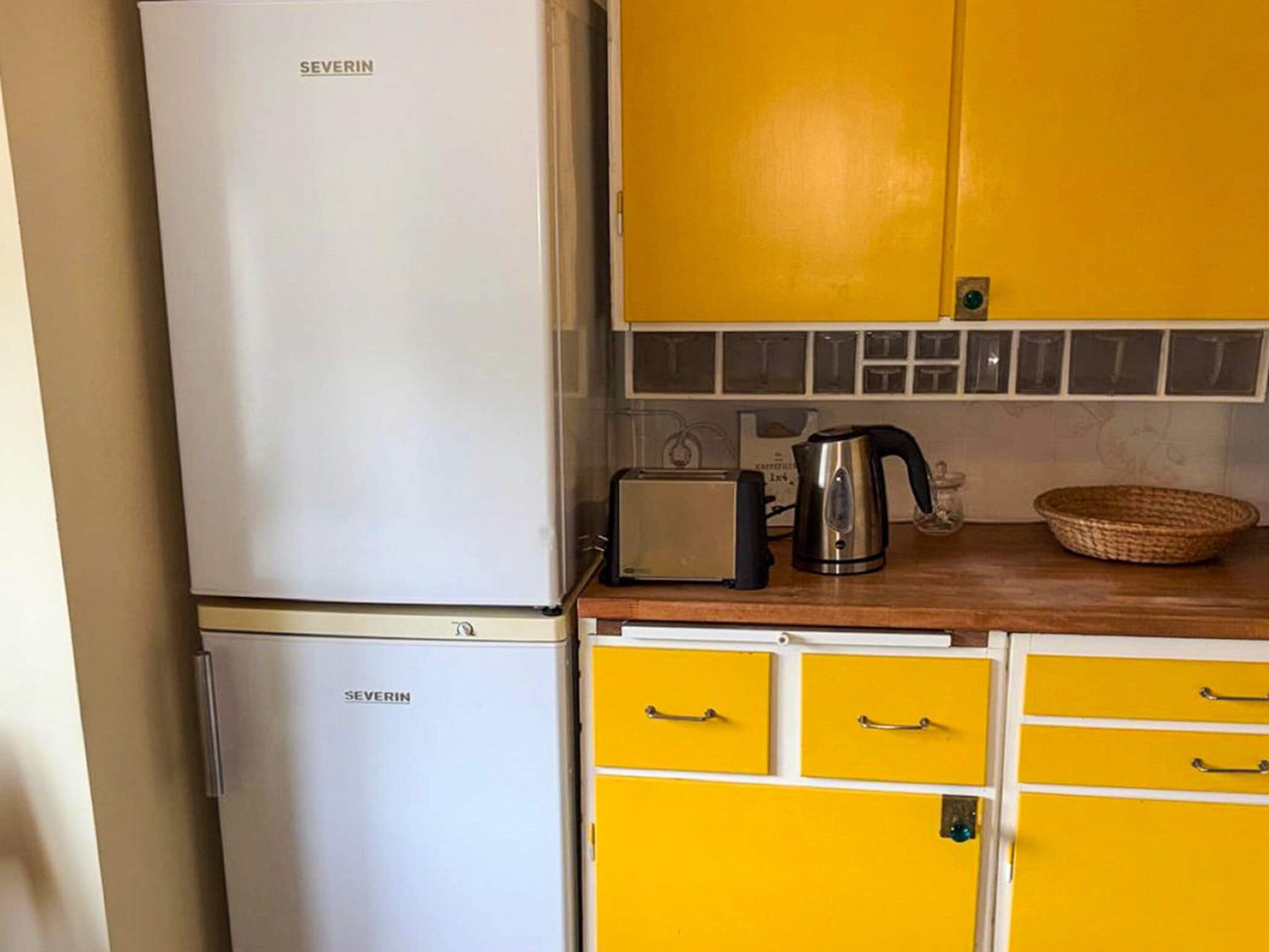 Una cocina con un refrigerador blanco, un tostador, una tetera y armarios amarillos.