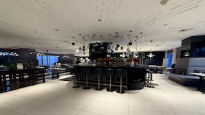 A modern bar area with a central bar, multiple seating options, and a ceiling with unique lighting fixtures.