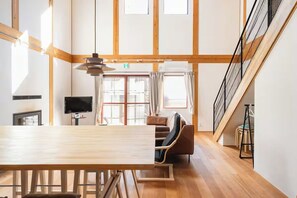 Ein geräumiges Zimmer mit Esstisch aus Holz, einer Couch, einem Fernseher und einer Treppe.