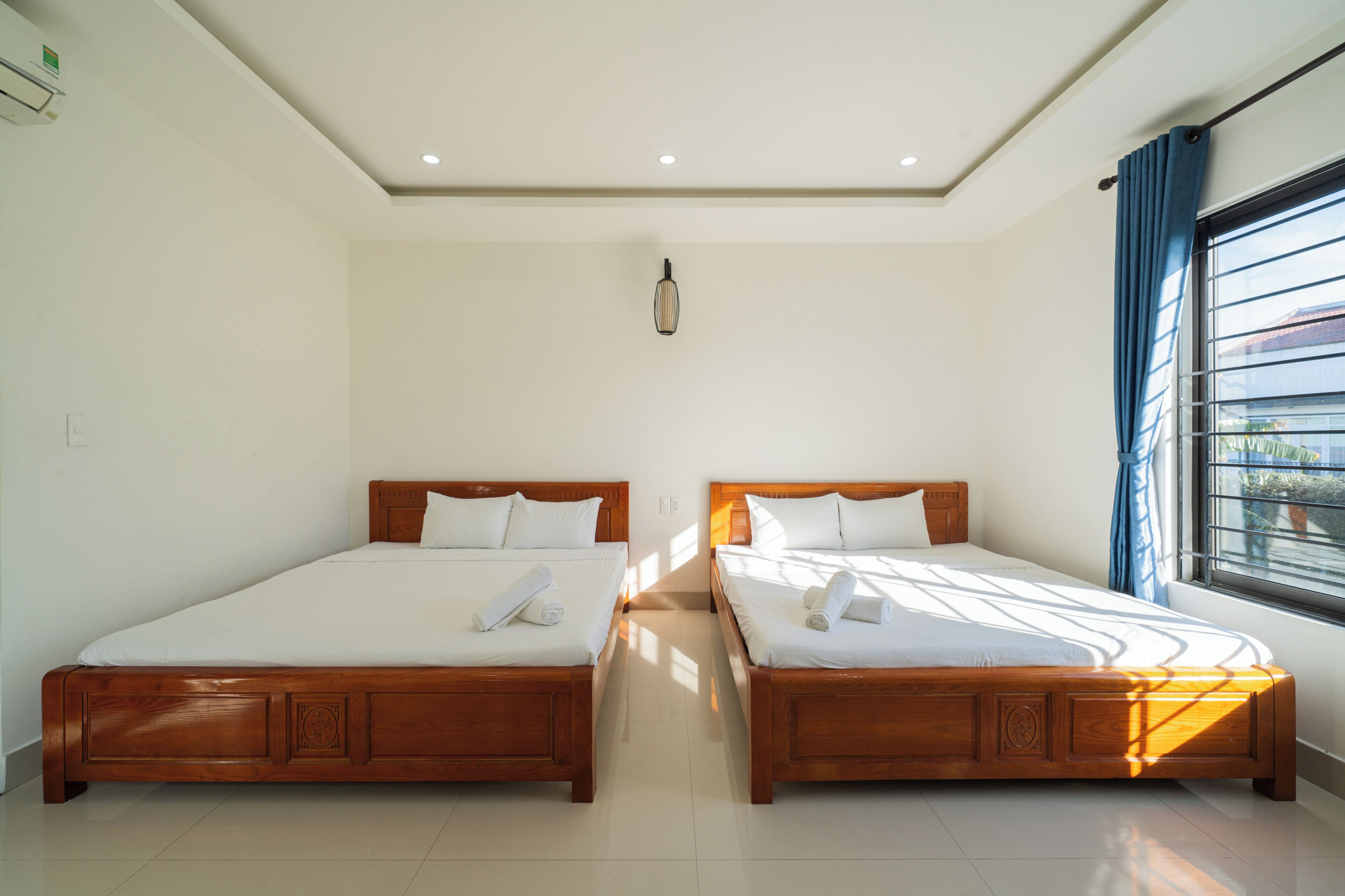 A hotel room with two wooden beds, a ceiling light, and a window with curtains.