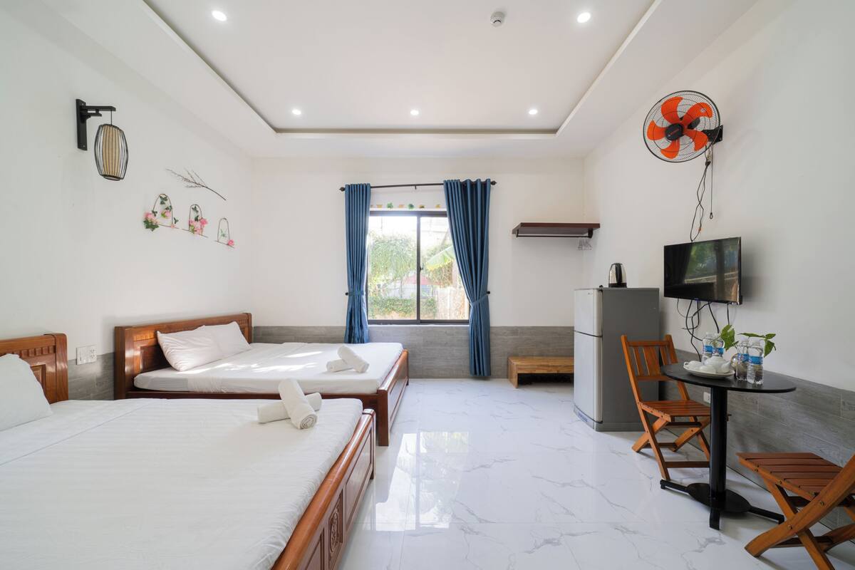 A hotel room with a bed, a desk with a chair, a TV, and a fan.