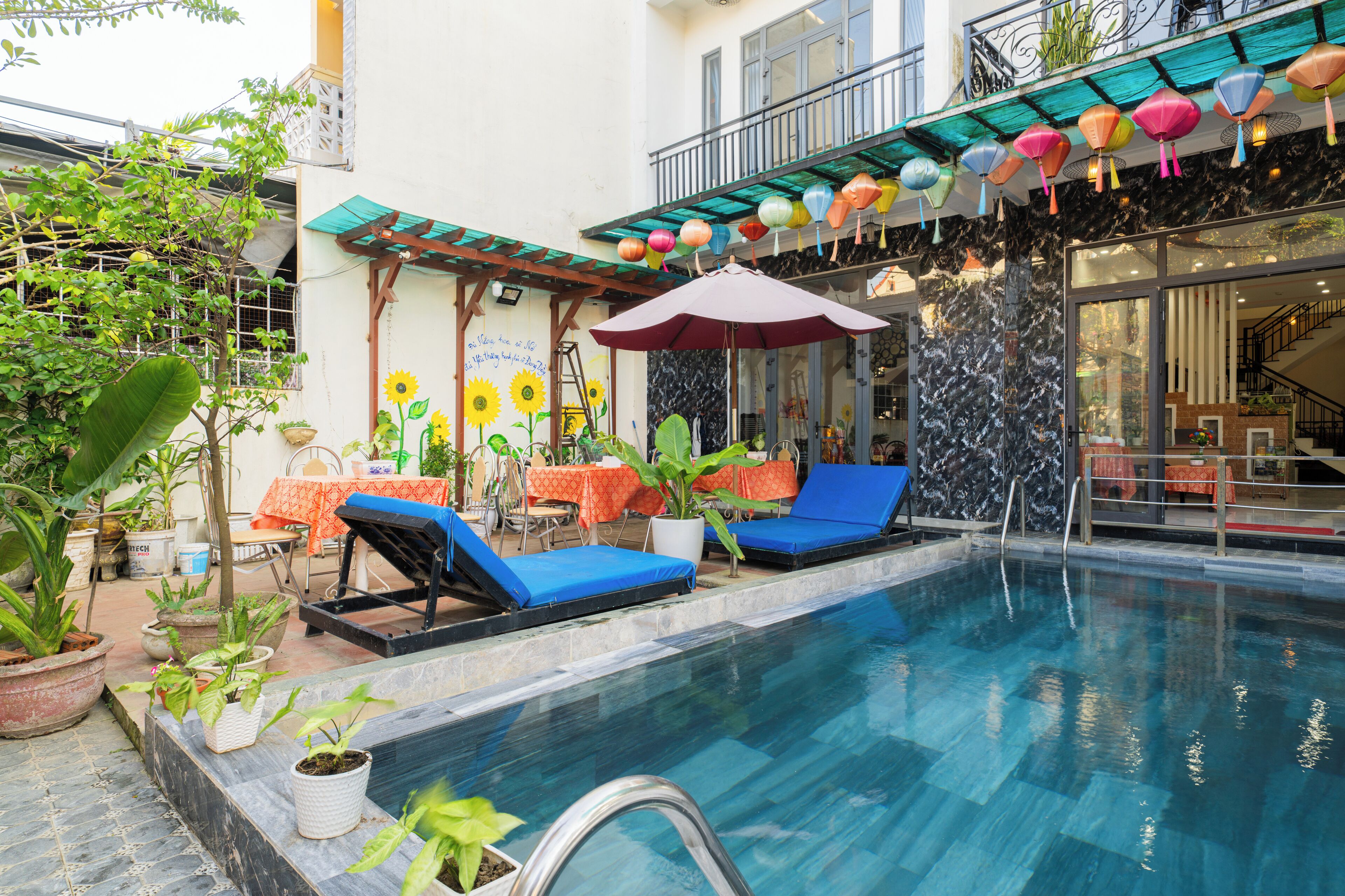 A pool area with lounge chairs, a table with an orange tablecloth, and potted plants.